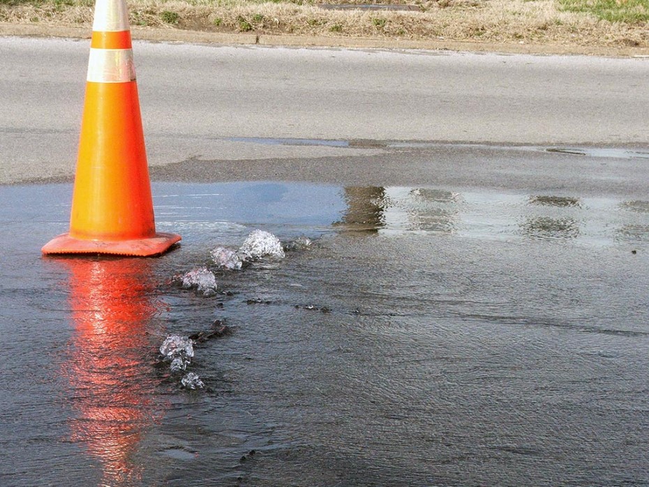 a pylon on a roadway where water is coming out of the ground